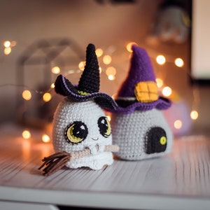 May include: Two crocheted Halloween decorations. One is a white ghost with a black witch hat and a broom. The other is a white house with a purple witch hat and a black door.