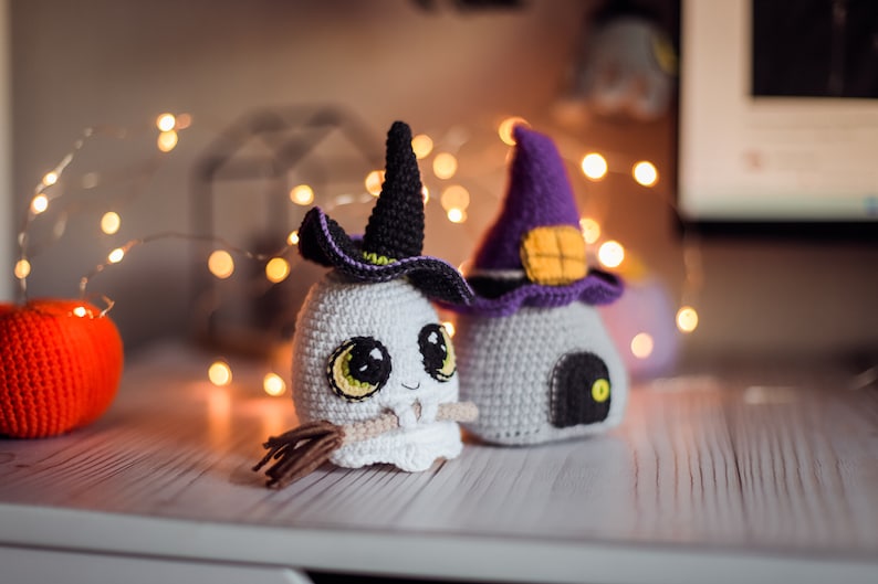 May include: Two crocheted Halloween decorations. One is a white ghost with a black witch hat and a broom. The other is a white house with a purple witch hat and a black door.