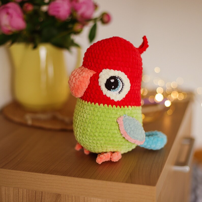 May include: A crocheted parrot toy with red, green, and blue accents. The parrot has a large, white eye with a blue pupil.