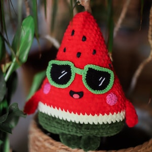 Puede incluir: Un juguete de peluche de sand&iacute;a rojo tejido a crochet que lleva gafas de sol verdes con una cara feliz. La sand&iacute;a tiene una c&aacute;scara verde y semillas negras.