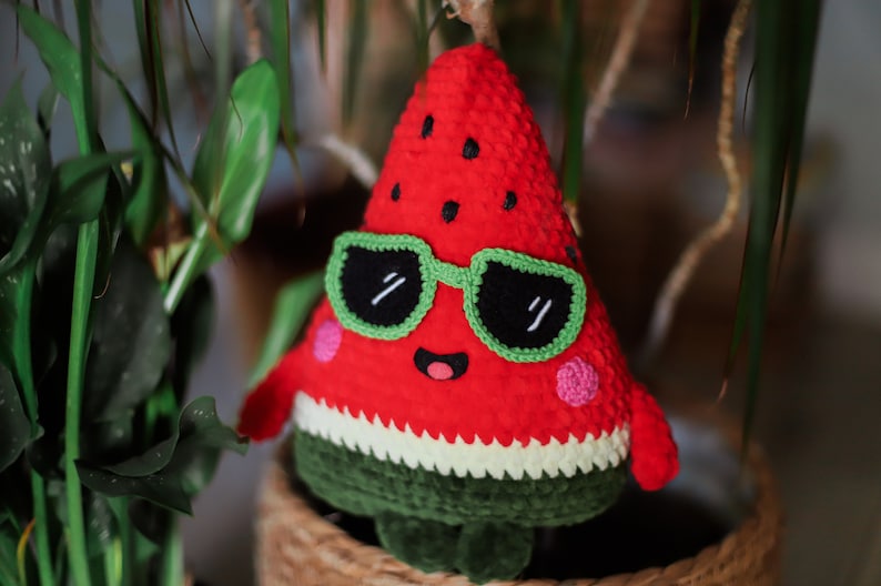 Puede incluir: Un juguete de peluche de sand&iacute;a rojo tejido a crochet que lleva gafas de sol verdes con una cara feliz. La sand&iacute;a tiene una c&aacute;scara verde y semillas negras.