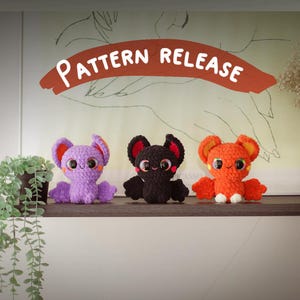 Puede incluir: Tres peluches de murci&eacute;lago de crochet en morado, negro y naranja. Los murci&eacute;lagos tienen ojos grandes y est&aacute;n sentados en un estante. El texto "PATTERN RELEASE" est&aacute; escrito en un arco rojo sobre los murci&eacute;lagos.
