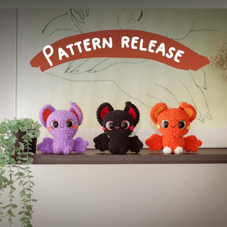 Puede incluir: Tres peluches de murci&eacute;lago de crochet en morado, negro y naranja. Los murci&eacute;lagos tienen ojos grandes y est&aacute;n sentados en un estante. El texto "PATTERN RELEASE" est&aacute; escrito en un arco rojo sobre los murci&eacute;lagos.