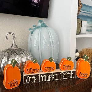 May include: A wooden sign reading Our Pumpkin Patch with five orange pumpkin-shaped cutouts attached to the front. Each pumpkin is personalized with the names Teddy, Katherine, Zyaire, Olivia, and Gracie in black script lettering.