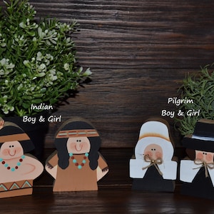 May include: Four wooden cutout figures featuring two characters labeled Indian Boy & Girl and two characters labeled Pilgrim Boy & Girl. The figures are painted with distinct facial features, clothing details, and accessories in various colors.