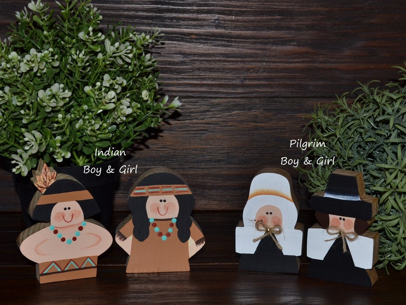 May include: Four wooden cutout figures featuring two characters labeled Indian Boy & Girl and two characters labeled Pilgrim Boy & Girl. The figures are painted with distinct facial features, clothing details, and accessories in various colors.