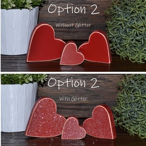 May include: Three red wooden hearts, one large, one medium, and one small, with the option of glitter or no glitter. The hearts are arranged in a row on a wooden surface. The text "Option 2" is written above the hearts, with the words "Without Glitter" or "With Glitter" written below the hearts.