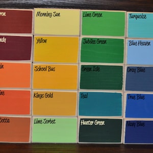 May include: A collection of small, rectangular wooden blocks, each painted a different color. The blocks are labeled with color names like "White," "Red Iron," "Morning Sun," and "Lime Green." The color palette includes a variety of hues, from vibrant to muted.