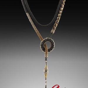 May include: A black, silver and gold beaded necklace with a knotted loop and a dangling pendant. The pendant is a silver and gold orb with intricate details. The necklace is labelled "Aasia Elegant Art Jewellery".