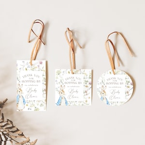 May include: Three baby shower gift tags with leather string hangers. The tags feature a watercolor illustration of Peter Rabbit and floral accents. Text on the tags reads "Thank you for hopping by to celebrate Baby Oliver."