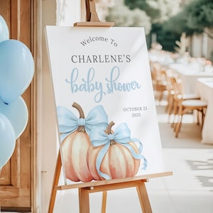 May include: A white rectangular sign on a wooden easel featuring the text Welcome To CHARLENE'S baby shower OCTOBER 25 2025. The sign displays two watercolor pumpkins with light blue bows. A cluster of light blue balloons is positioned to the left.