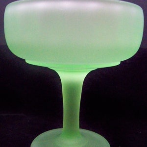 May include: A frosted green glass pedestal bowl with a wide, round base. The bowl is made of a translucent glass with a frosted finish.