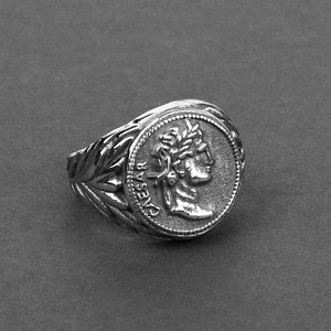 May include: Silver ring with a detailed design featuring a profile of a person wearing a laurel wreath. The ring has the word "CAESAR" inscribed on the side.