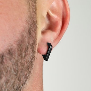 May include: A pair of black square hoop earrings. The earrings are made of a smooth, matte material and have a simple, modern design.