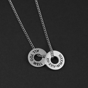 May include: A silver chain necklace with two circular pendants. The pendants are engraved with the words "All Too Well" and "XII. XXV. MMXX".