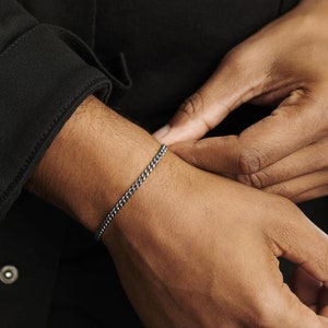 May include: A silver chain bracelet on a person's wrist.