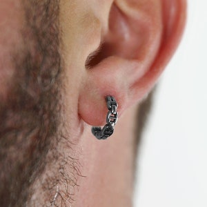 Puede incluir: Un pendiente de aro de cadena de plata. El pendiente se lleva en la oreja izquierda de una persona con barba.