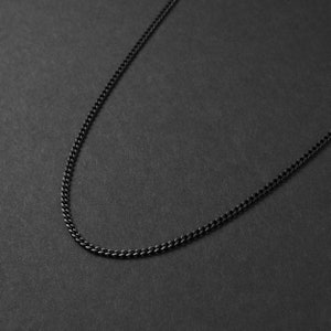 May include: A black chain necklace on a black background.