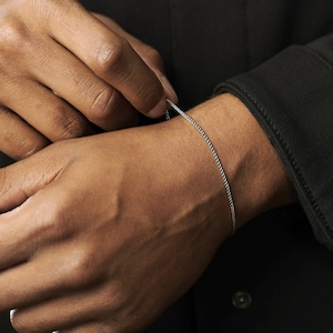 May include: A silver chain bracelet on a person's wrist.