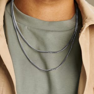 May include: Two silver chain necklaces layered on a person's neck. The chains are both curb style and have a shiny finish.