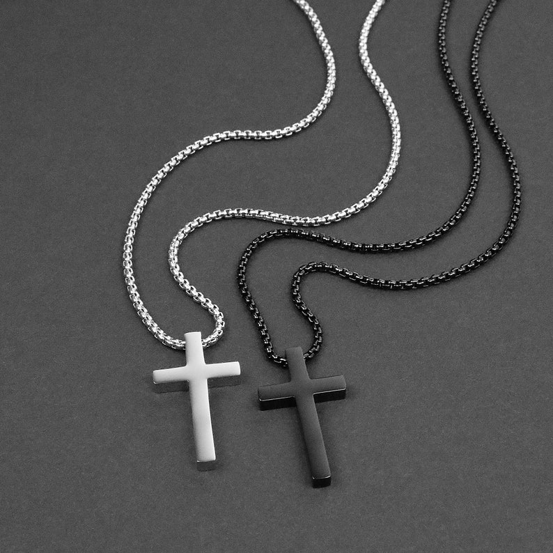 May include: Two silver chains with cross pendants, one black and one silver, on a gray background.