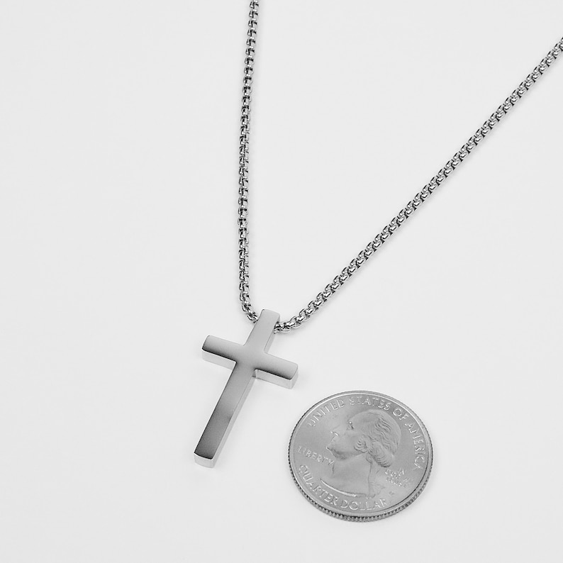May include: A silver chain necklace with a silver cross pendant. The cross is about the size of a US quarter.