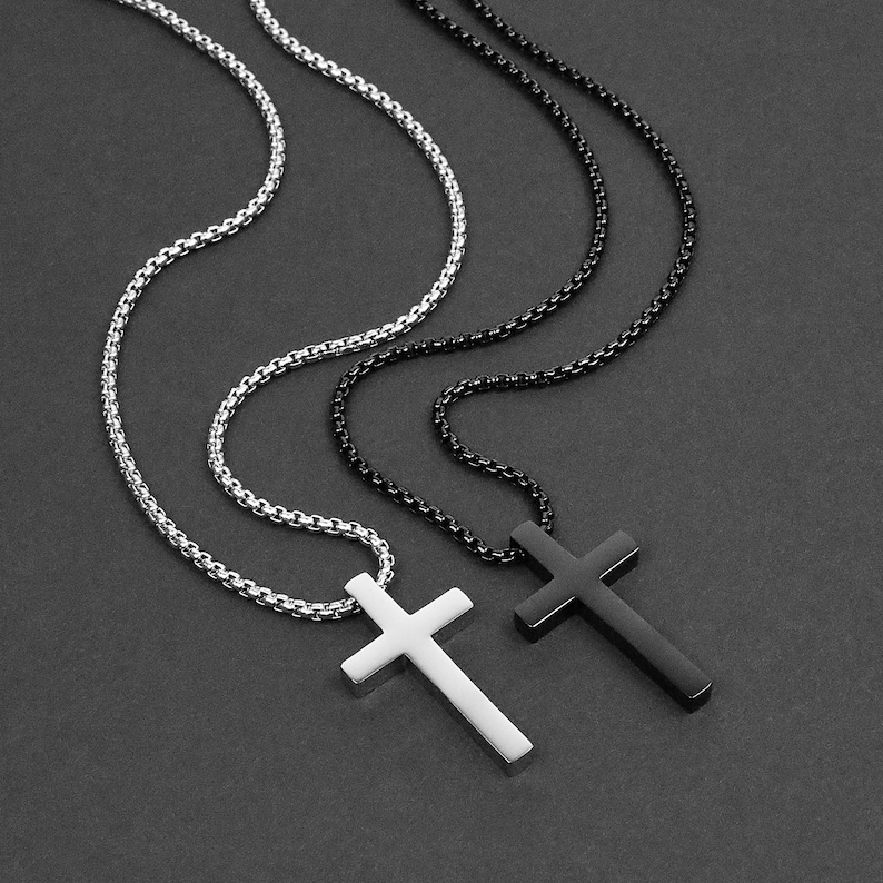 May include: Two silver chain necklaces with cross pendants. One cross is silver and the other is black.