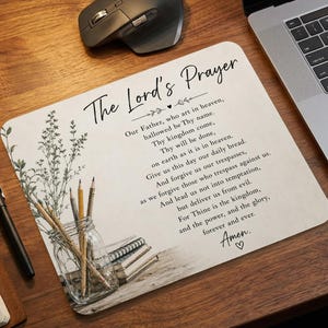 May include: A rectangular mouse pad featuring the text of The Lord's Prayer in black script. The design includes a botanical illustration of a sprig in a glass jar with pencils and a stack of books, set against a light, textured background.