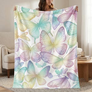 May include: A white blanket featuring a repeating pattern of watercolor butterflies in pastel colors. The butterflies are in shades of yellow, blue, purple, and pink. The blanket is soft and cozy, perfect for snuggling up on the couch or bed.