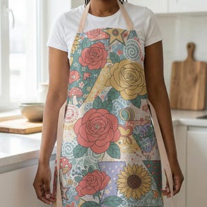 May include: A colorful apron with a floral patchwork design. The apron features large roses, sunflowers, and whimsical mushroom and star motifs in shades of pink, yellow, and blue. The apron has a light pink neck strap and waist ties.