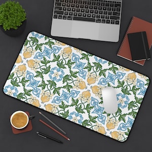 May include: A rectangular desk mat with a white background and a repeating pattern of yellow lemons, blue floral designs, and green leaves. The mat has a black border and is designed to accommodate a mouse and keyboard.