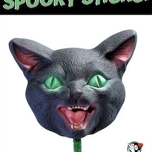 May include: A Halloween-themed black cat head on a green stick, with glowing green eyes and an open mouth. The text "SPOOKY STICKS!" is at the top, and "BLACK CAT" is at the bottom. The Pulp Novelties logo is in the bottom right corner.