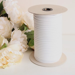 May include: A spool of white elastic cord, wound around a cardboard core. The cord is approximately 1/4 inch wide.