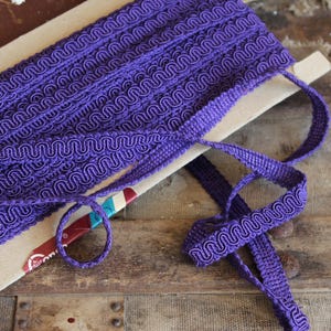 May include: Purple trim with a wavy pattern. The trim is on a cardboard backing and is folded in half.