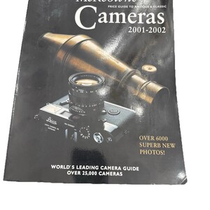May include: A book titled "McKeown's Cameras 2001-2002" with a black cover. The cover features a vintage camera and a brass telescope. Text on the cover includes "World's Leading Camera Guide" and "Over 6000 Superb New Photos!"