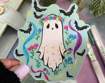May include: A sticker featuring a white ghost with a floral crown and a light blue background. The ghost is surrounded by bats, flowers, and ribbons in various colors.