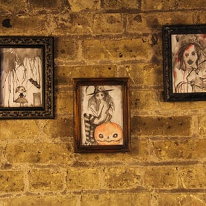 Peut inclure: Trois dessins en noir et blanc encadr&eacute;s sur un mur de briques. Les dessins repr&eacute;sentent une femme avec une citrouille, une femme avec un chapeau et une femme avec un oiseau.