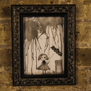 May include: A framed black and white watercolor painting of a girl holding a string attached to a bat. The background is a dark gray with splatter paint and drips. The girl is wearing a dress and has a bow in her hair. The bat is flying in the air. The painting is in a black frame with ornate details.