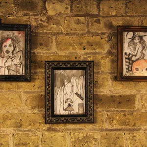 May include: Three framed drawings on a brick wall. The drawings are in black and white and feature a woman with long hair, a girl with a pumpkin, and a girl with a bird.