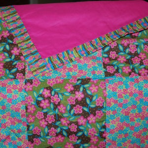 Puede incluir: Un edredón de patchwork con un vibrante estampado floral. El edredón presenta cuadrados de tela en rosa, azul, verde y marrón, con una capa superior rosa lisa. El diseño floral incluye flores rosas y detalles azules.