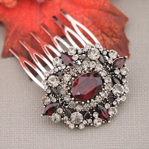 May include: A silver hair comb with a large red and clear rhinestone design. The comb has a decorative floral pattern with a large oval-shaped red rhinestone in the center.