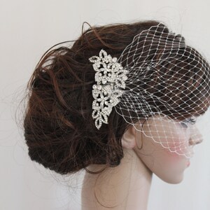 May include: A white bridal veil with a delicate net pattern and a silver rhinestone hair comb. The comb features a floral design with intricate details.