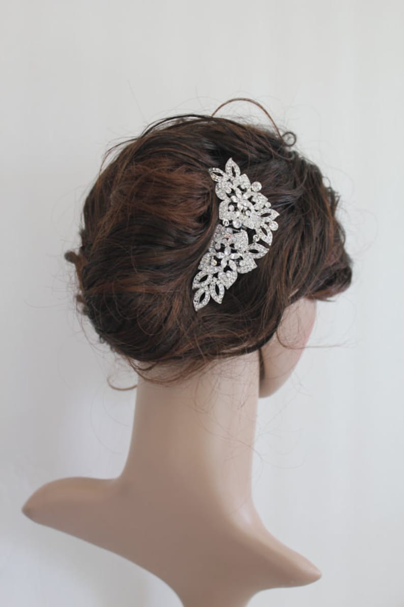 May include: Silver hair comb with a large, ornate design featuring clear rhinestones. The comb is shown in a model's hair.