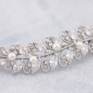 May include: Silver hair clip with a leaf design and clear and pearl-like embellishments.
