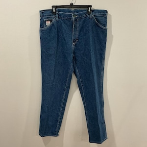 May include: Blue denim jeans with a classic five-pocket design. The jeans have a straight leg cut and a button and zipper closure. A small patch is visible on the front pocket.