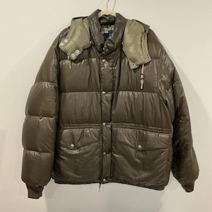May include: A brown puffer jacket with a hood. The jacket has a quilted design, a button-up front, and two front pockets. The hood is a lighter shade of green. The jacket is hanging on a hanger.