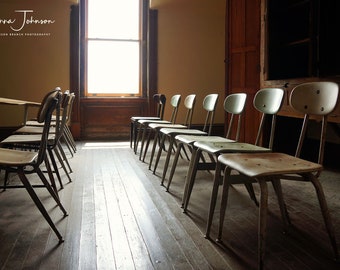 May include: A classroom with rows of vintage metal and wood chairs. The chairs are arranged in rows facing a window. The room has a wooden floor and a wooden door in the background. The chairs are all in good condition and have a light green paint finish.