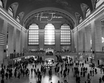 May include: Black and white photo of the interior of Grand Central Station in New York City. The photo shows the main concourse with a large arched ceiling and a large window at the far end. There are many people walking around the concourse. The text "Hanna Johnson, Johnson Branch Photography" is in the upper center of the image.
