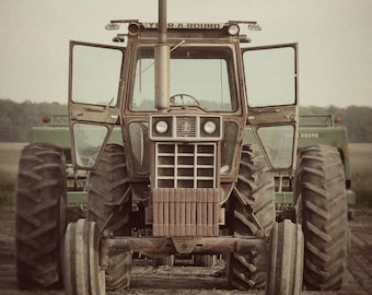May include: A red and green tractor with large tires and a "Year-Round" sign on the cab. The tractor is in a field with a brown, dirt background.
