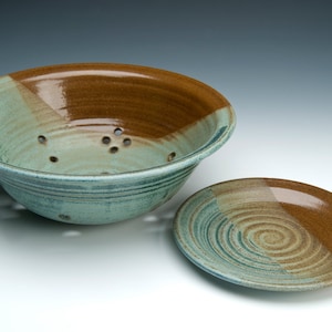 May include: A brown and green ceramic colander with a matching plate. The colander has a brown rim and a green interior with a brown stripe around the top. The plate has a brown rim and a green interior with a brown stripe around the top.